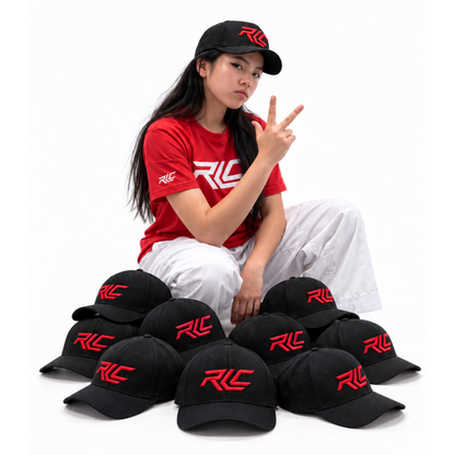 A woman sits on a white studio background wearing a red T-shirt and white pants, with multiple black baseball caps featuring a red 'RLC' logo arranged around her. The product appears to be the branded caps, shown both worn and stacked.